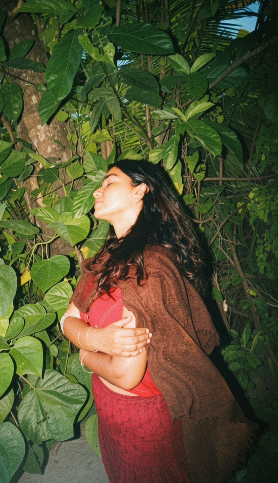 Tara with eyes closed among dense green foliage, wrapped in a brown shawl