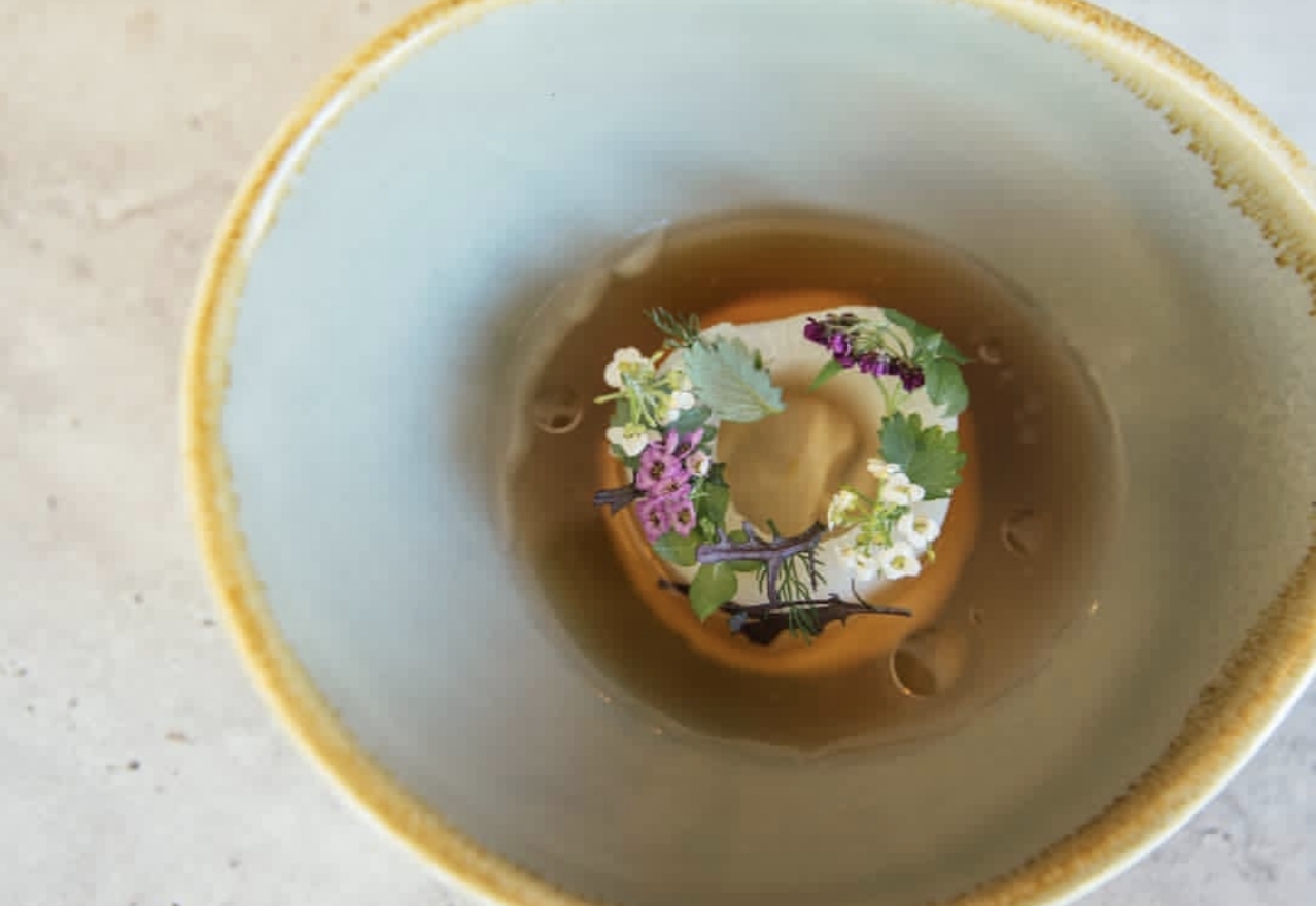 A refined broth course garnished with fresh flowers and herbs